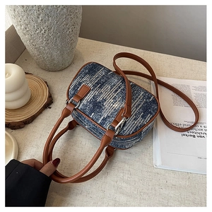 Detailed view of blue denim square handbag with silver sequins and brown leather straps