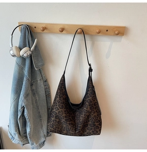 Detail der Hobo-Tasche mit Leopardenmuster, hängend an Haken mit Freizeitkleidung