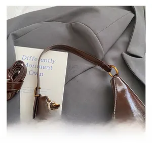 Détail macro du sac hobo en cuir verni marron foncé avec un joli pendentif ours en peluche