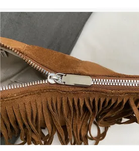 Detail shot of a brown suede bag featuring a smooth silver metal zipper and long fringes