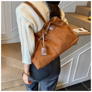 Détail d'un grand sac cabas en daim marron avec des anses en cuir lisse et texture mate
