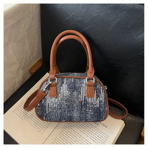 Detail of blue denim sequins handbag showing brown leather handles on a book