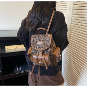 Détail du sac à dos léopard montrant les finitions en similicuir brun et la boucle en métal