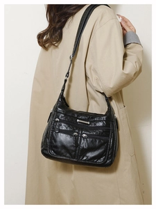 Detailed view of black litchi textured leather shoulder bag with multiple zippers