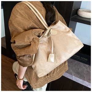 Détail du sac cabas en daim beige avec fines anses et design minimaliste porté par un mannequin