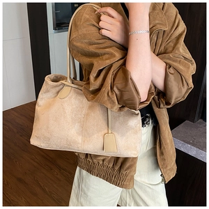 Détail du sac cabas en daim beige avec poignées fines et étiquette décorative
