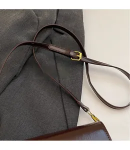 Détail d'un sac bandoulière en cuir marron foncé avec sangle réglable et boucle en métal doré