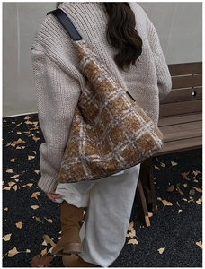 Close-up of brown plaid fuzzy tote bag with leather strap in a warm autumn street setting