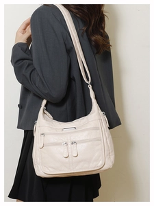 Detail view of beige soft leather crossbody bag featuring multiple functional zipper pockets