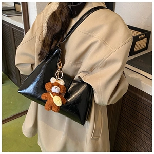 Détail d'un sac à bandoulière noir brillant avec un charmant ours en peluche marron