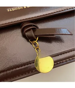 Détail d'un sac en cuir marron vintage avec nœud décoratif et pendentif doré rond