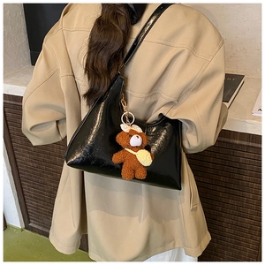 Détail d'un sac à bandoulière noir brillant avec un pendentif ours en peluche marron