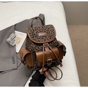 Détail du sac à dos léopard avec garniture en cuir et boucles métalliques sur lit blanc
