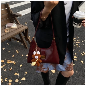 Détail du sac sous le bras bordeaux brillant avec un petit ours en peluche marron en ville