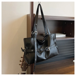 Dettaglio borsa tote in ecopelle nera con occhielli argentati e fibbie su scaffale in legno
