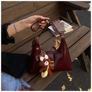 Détail d'un sac à main bordeaux en cuir brillant avec un charm chien en peluche sur un banc