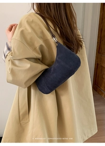 Borsa a mezzaluna in camoscio blu scuro indossata da una modella con trench beige