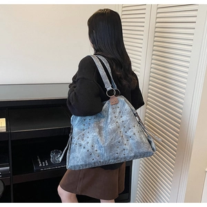 Détail du sac cabas en denim délavé bleu clair avec rivets métalliques et zip à pompon