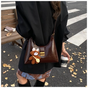 Détail d'un sac d'épaule en cuir ciré marron foncé avec un petit ours en peluche