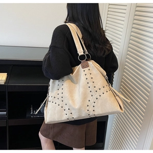 Détail d'un grand sac cabas beige orné de clous métalliques et de pompons latéraux
