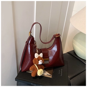Détail du sac croissant bordeaux en cuir ciré avec une breloque d'ours en peluche