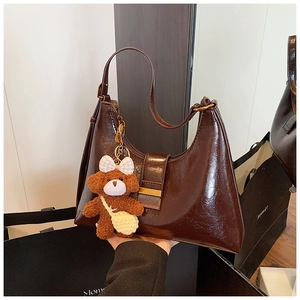Détail d'un sac hobo en cuir marron brillant avec pendentif ours et boucles dorées