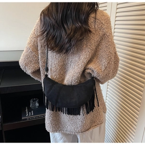 Detailed view of black suede crescent bag with long fringe tassels and knot strap detail
