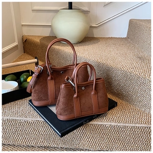 Detail view of large and small brown suede bucket bags with leather trim on steps