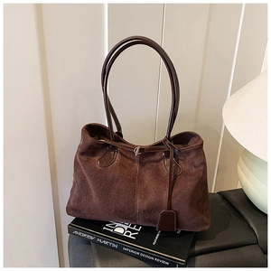 Détail macro du sac cabas en daim marron foncé avec coutures et fine bandoulière en cuir