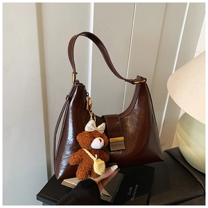 Détail d'un sac hobo en cuir brillant marron foncé avec breloque ours et boucle en métal