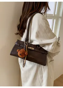 Detail of dark brown leather handbag featuring a gold buckle lock and plush bear charm