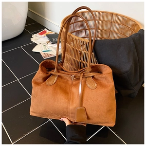 Gros plan du sac cabas en daim marron avec détails de surpiqûres et pendentif carré élégant