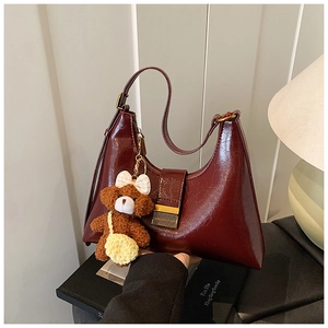 Détail du sac porté épaule en cuir bordeaux brillant avec une petite breloque d'ours