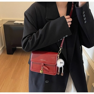 Détail du sac bandoulière en cuir verni bordeaux avec boucle dorée et bijou en peluche