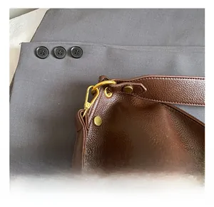 Close-up of golden metal hooks and textured leather strap on a large tote bag