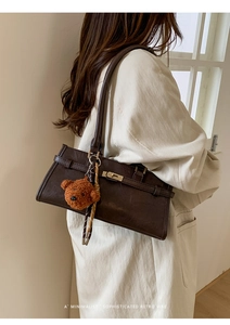Detail of retro dark coffee leather bag with metal buckle and teddy bear charm accessory