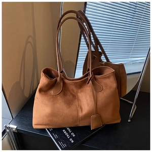 Détail du sac cabas en daim marron avec coutures verticales et étiquette en cuir sur le côté