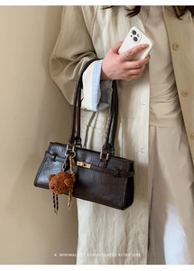 Detail of dark brown leather handbag with gold twist lock and cute teddy bear charm