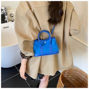 Detail of blue suede crossbody bucket bag with round metal buckle on lifestyle setting