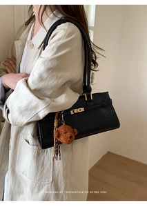 Close-up of black retro leather shoulder bag with gold clasp and plush bear charm