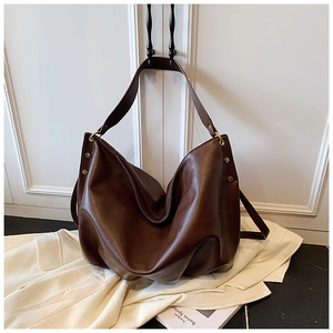 Detail of dark brown leather tote bag featuring gold rivets and textured litchi grain