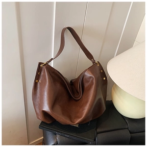 Detail view of a brown soft leather hobo bag featuring silver rivets and a wide shoulder strap