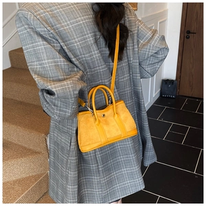 Lindy style bucket bag in ginger suede worn as a crossbody with grey suit