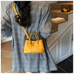 Detail of yellow mini bucket bag featuring mixed suede and leather texture on a grey blazer