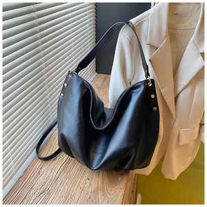 Detail of black pebbled leather hobo bag with gold studs on a wooden table surface
