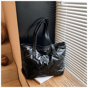 Detailaufnahme der schwarzen Stepptasche mit V-Steppmuster und Logo auf einer Holzbank