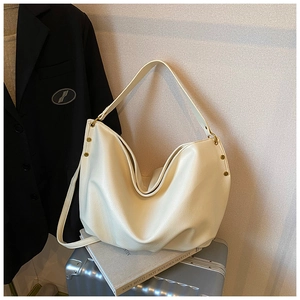 Detail of off-white tote bag showing pebbled leather texture and gold metal rivets