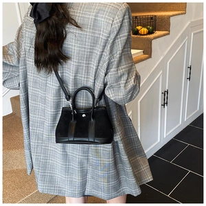 Detailed view of a black mini bucket bag with silver hardware worn with a grey plaid blazer