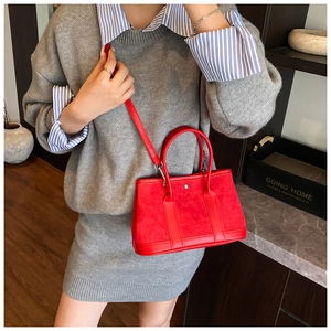 Red crossbody bucket bag shown on a model with striped shirt and gray knit skirt