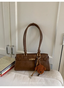 Detail view of vintage brown leather underarm bag with metal lock and teddy bear charm